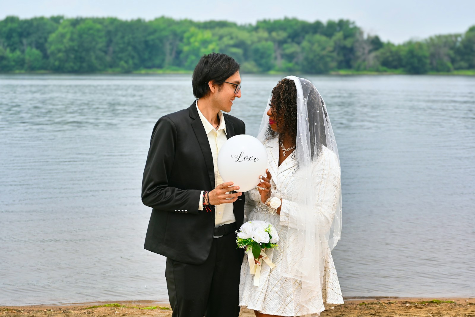 A bride and groom standing next to a body of water
